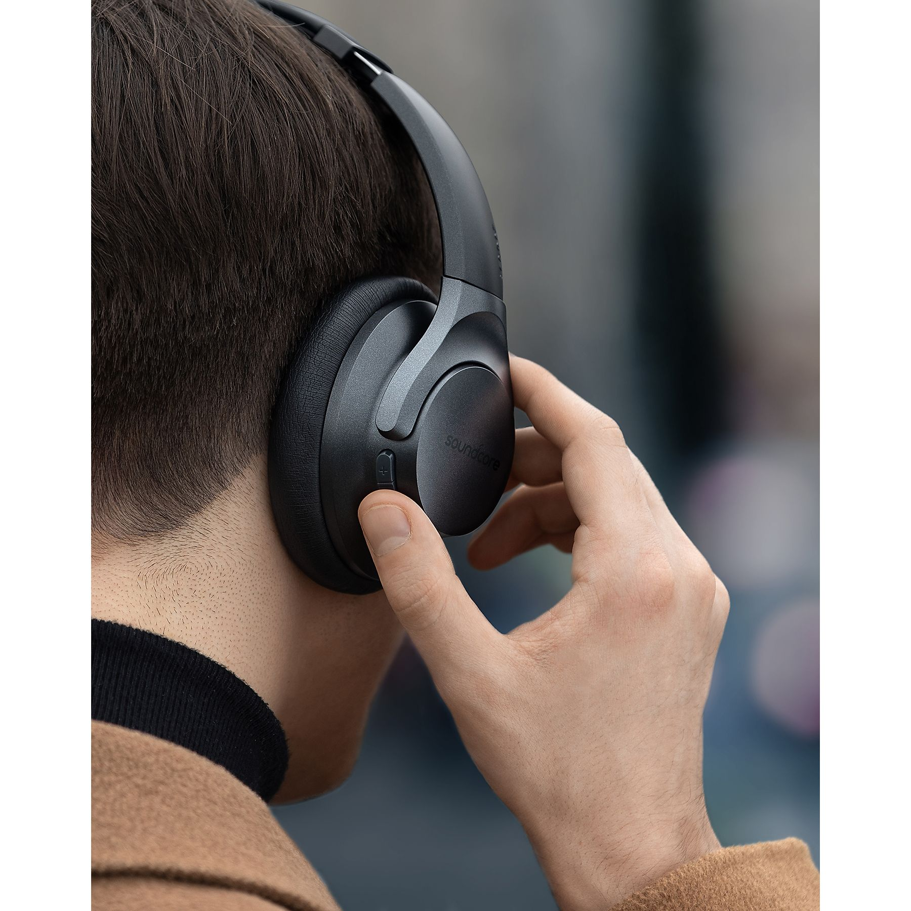 Mężczyzna z ciemnymi włosami nosi czarne słuchawki, jedną ręką dotyka ucha.