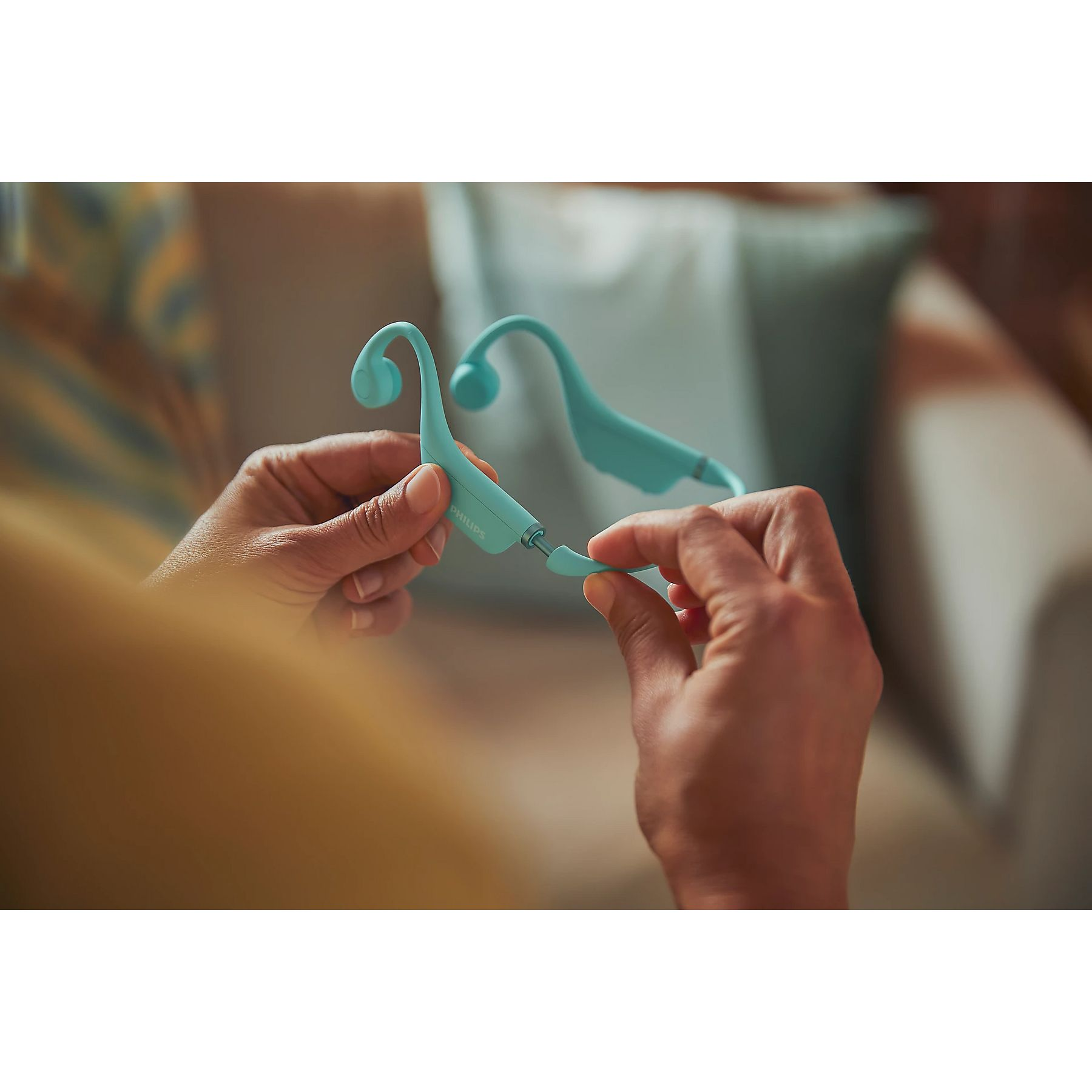 Dłonie trzymają turkusowe słuchawki, osoba je łączy.