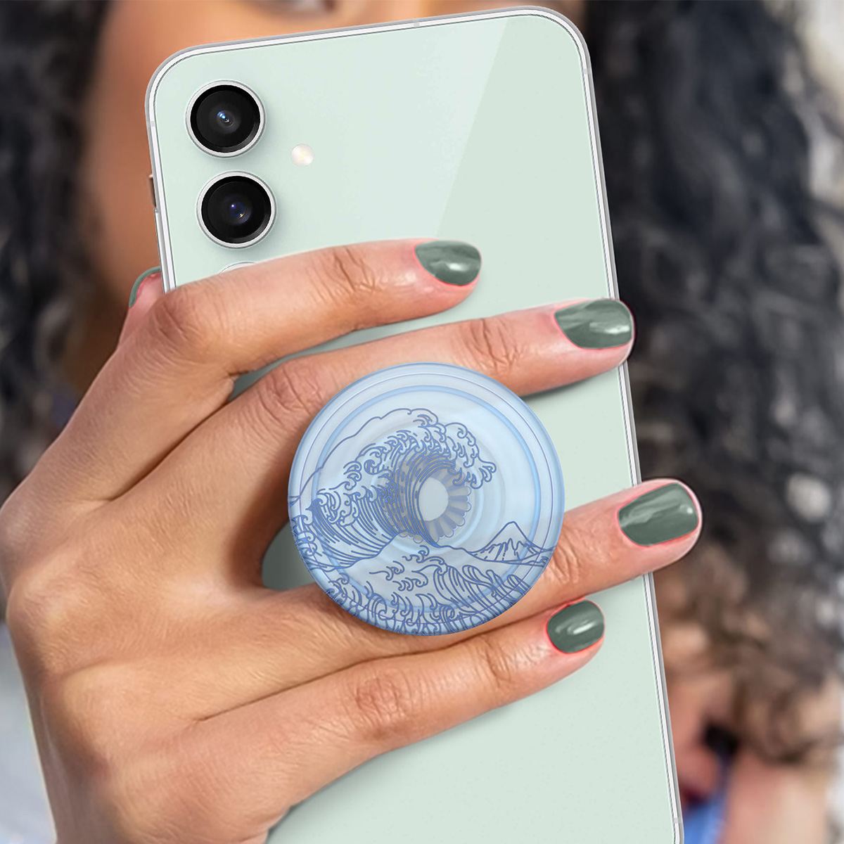 Una mano tiene un telefono verde chiaro con un pop socket a forma di onda blu.
