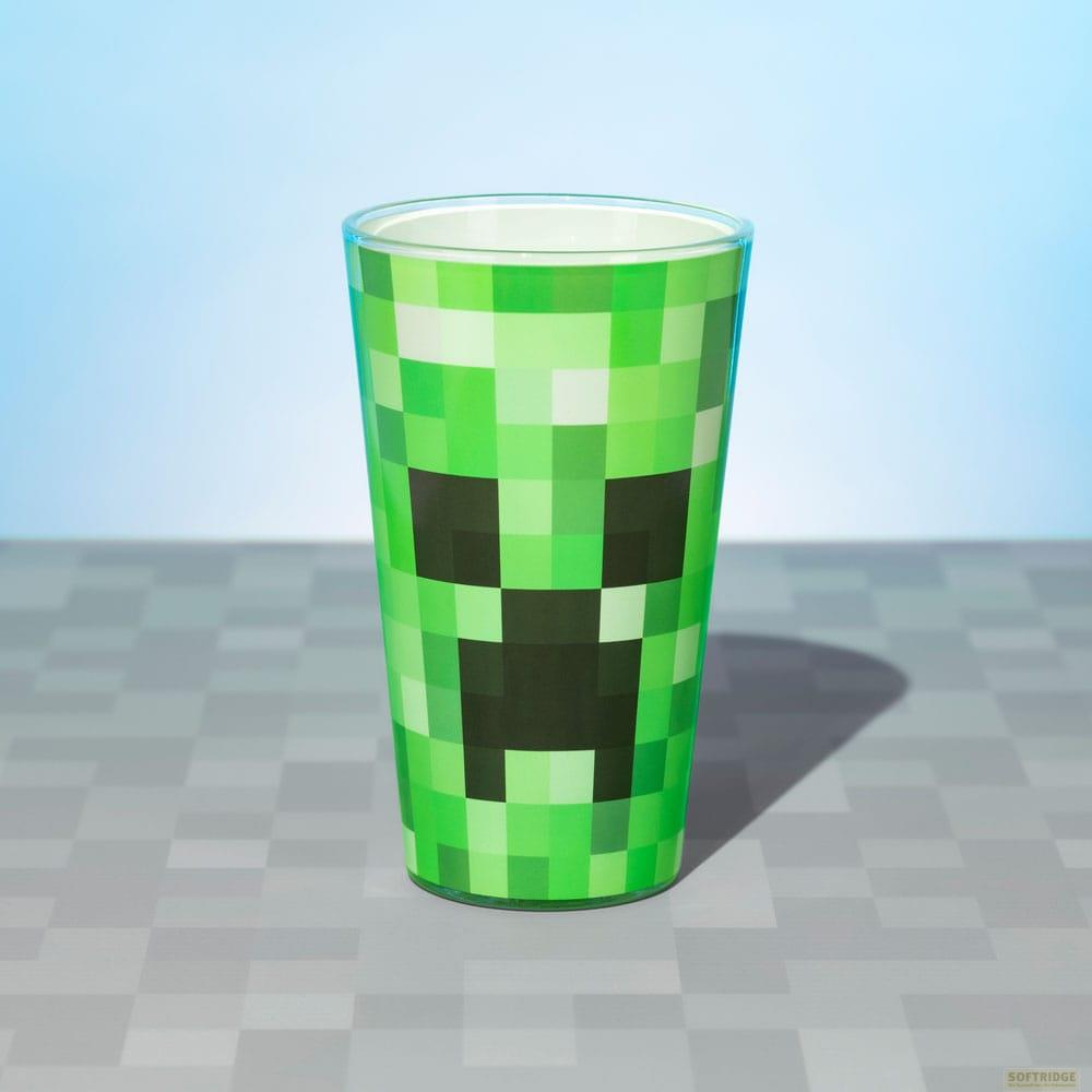 Zielony kubek ze wzorem twarzy Creepera z Minecraft, na kratkowanym blacie.