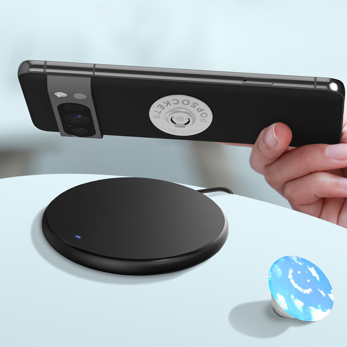Un telefono con PopSocket tenuto sopra un pad di ricarica wireless nero.