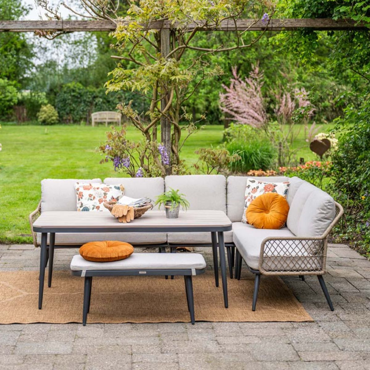 Canapé et table d'extérieur avec coussins sur patio pavé, fond de jardin verdoyant.