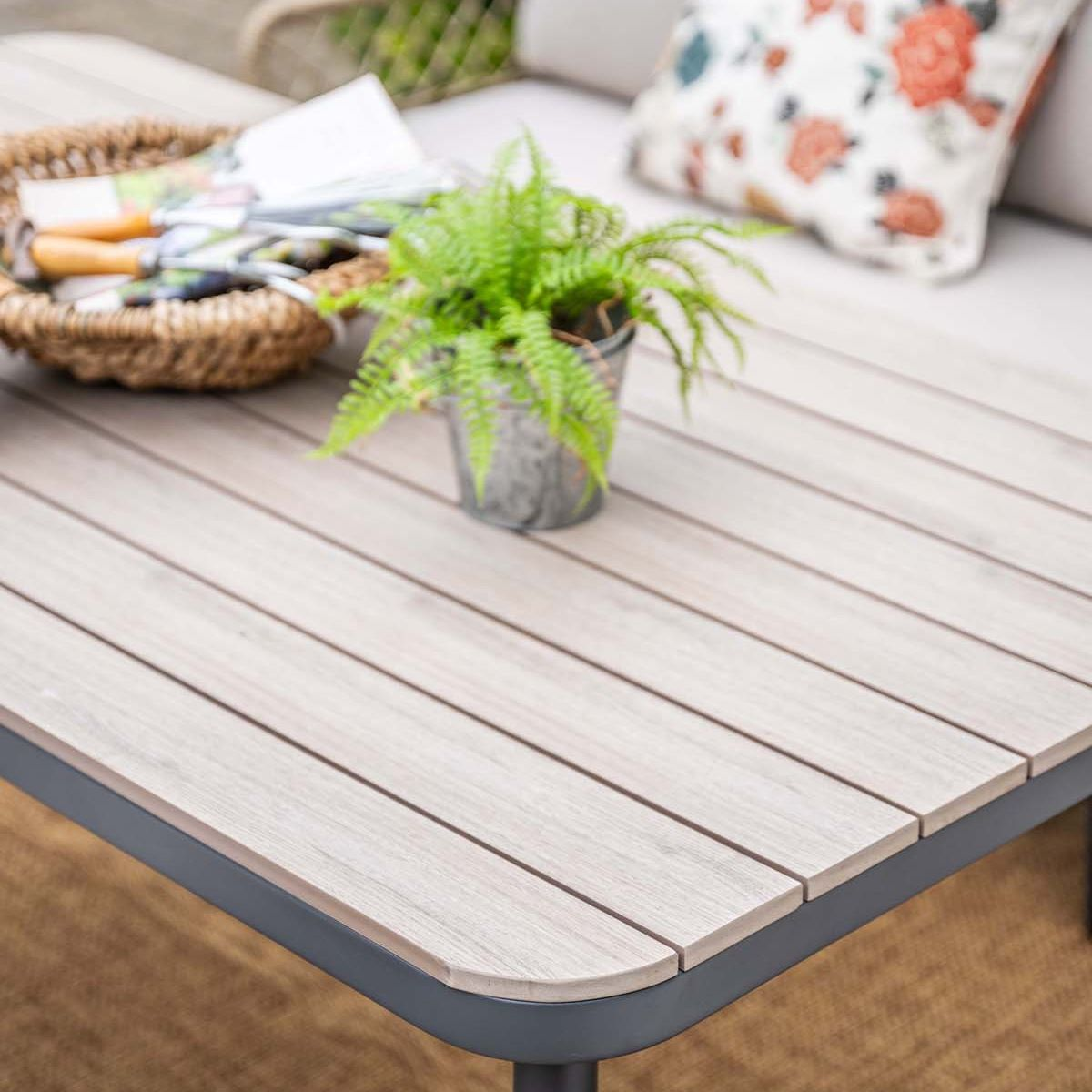 Table en bois avec panier, plante et coussin. Extérieur. Lumineux.