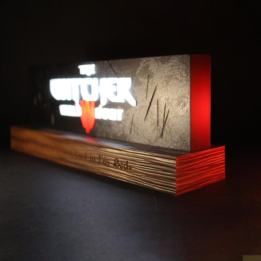 Un cartello luminoso con logo "The Witcher" su base di legno con illuminazione rossa.