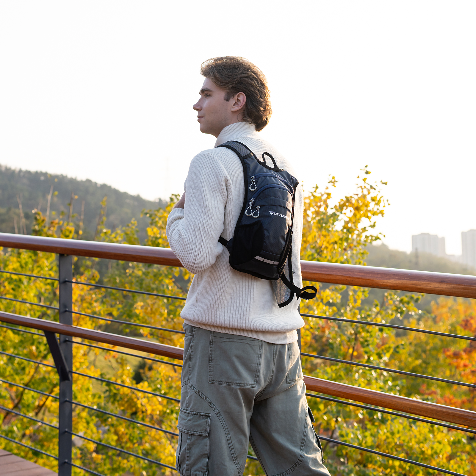 Mężczyzna w plecaku stoi na drewnianej kładce, patrząc na jesienne drzewa.