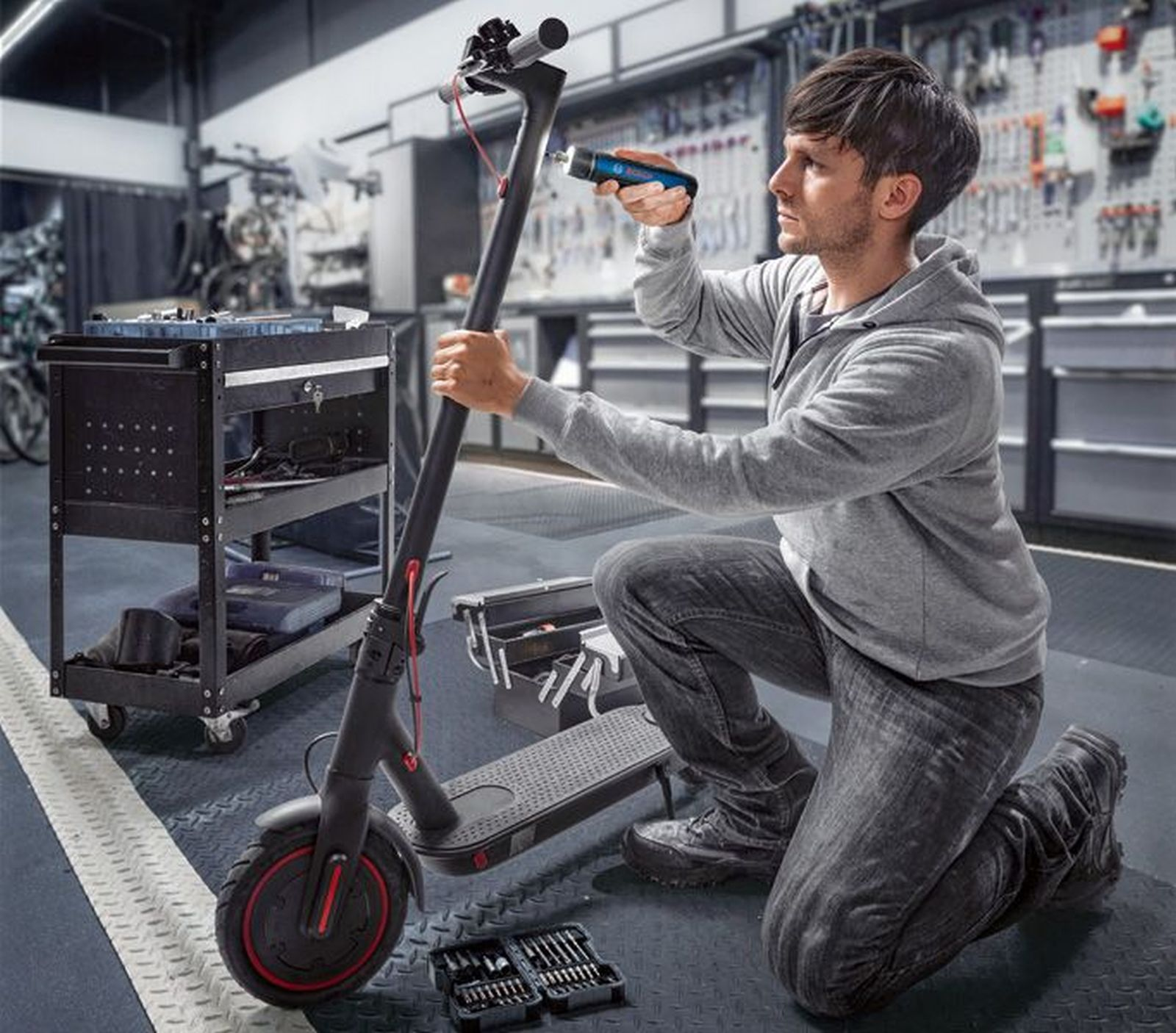 Adam atölyede aletlerle elektrikli scooter tamir ediyor.