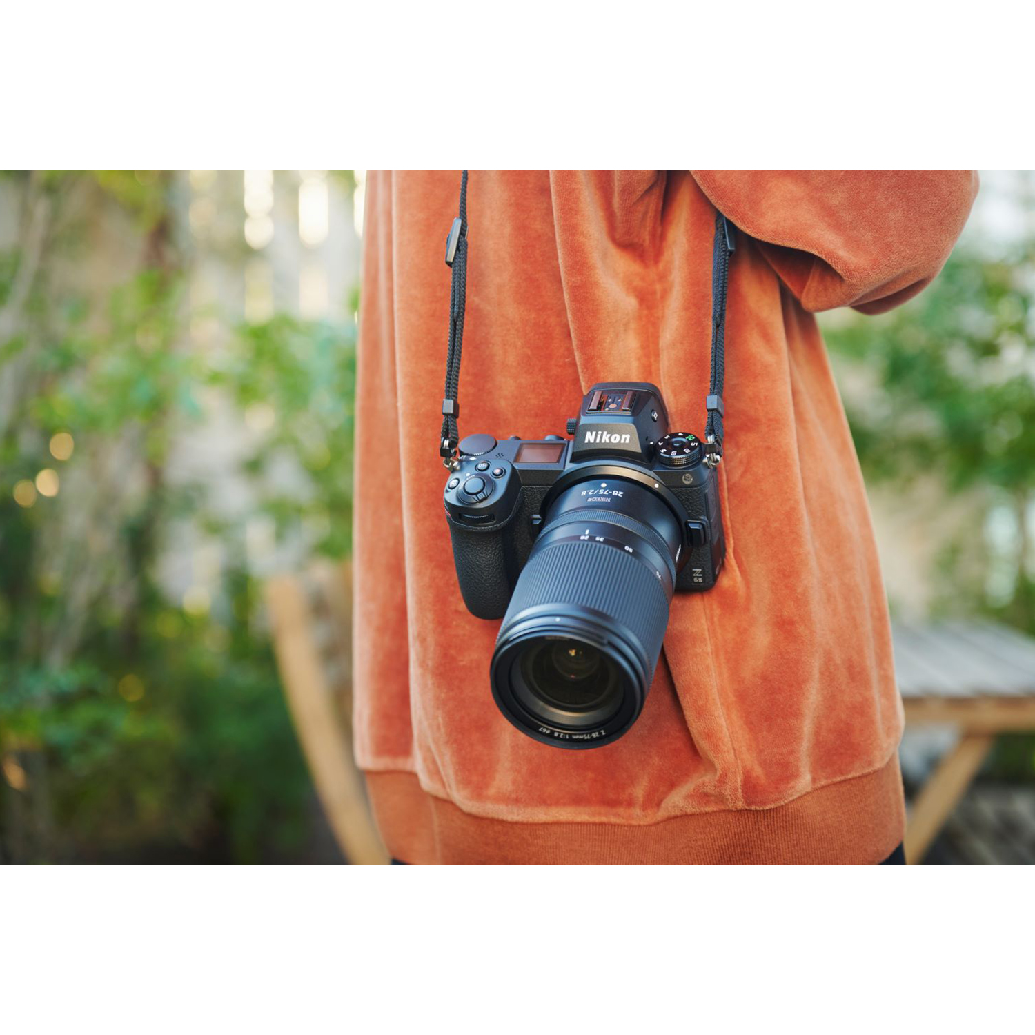 Una persona indossa una felpa arancione con una fotocamera Nikon al collo.