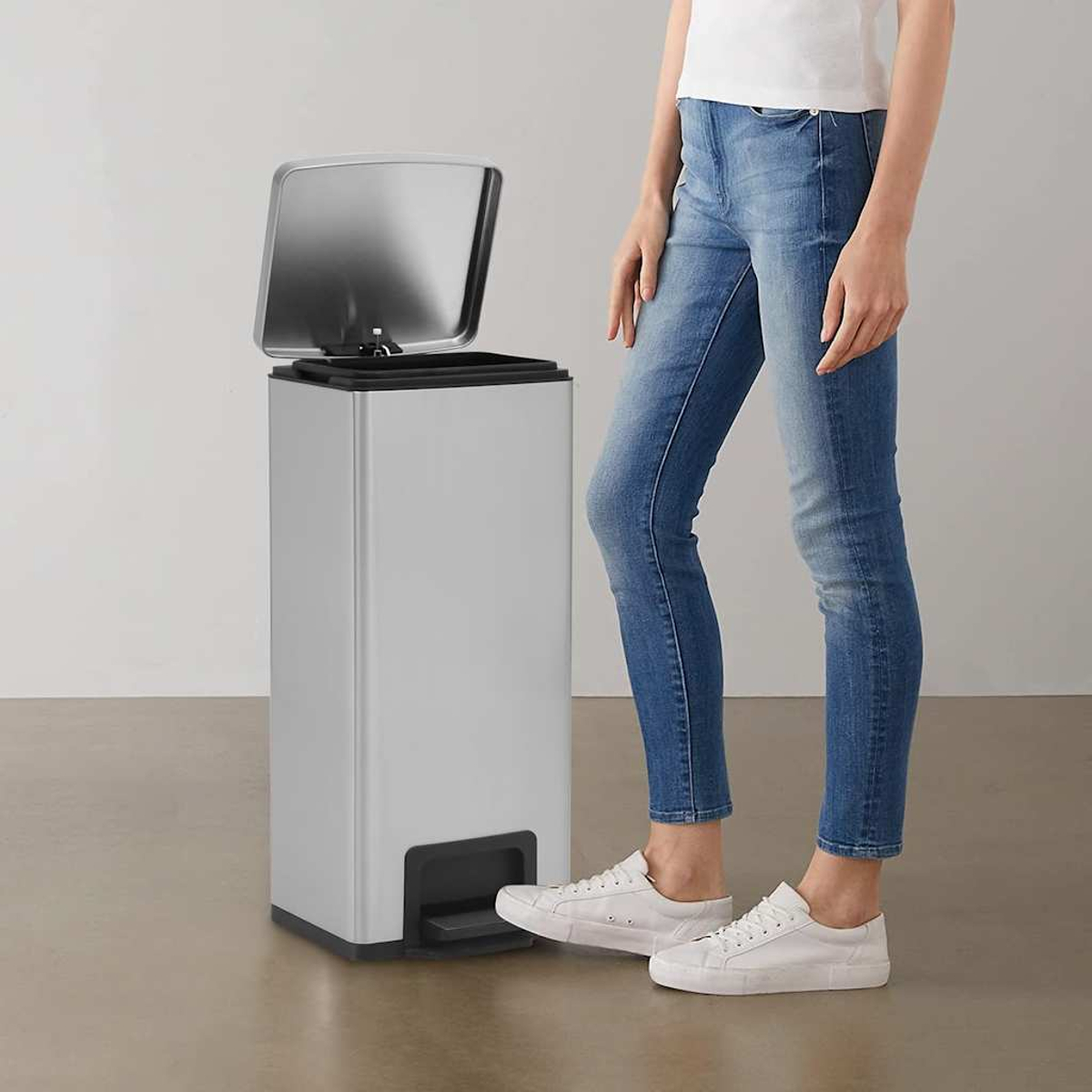 Eine Person in Jeans benutzt einen silbernen Mülleimer mit Pedal.