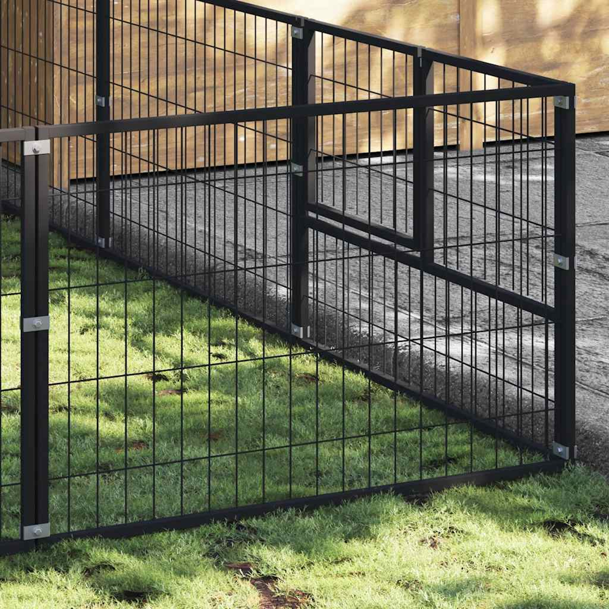 Ein schwarzer Metallzaun mit Gitterstruktur steht auf Gras und Kies.