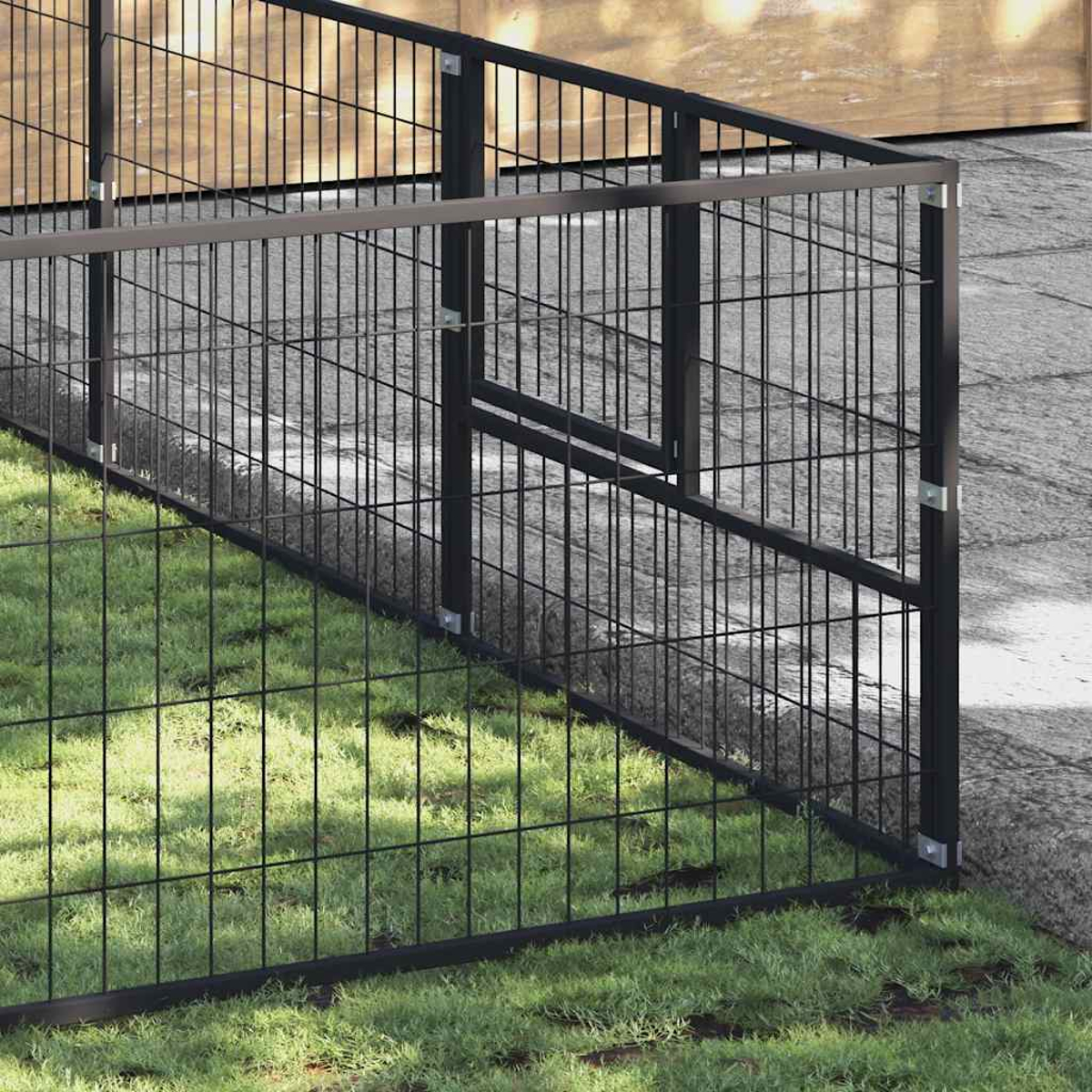 Ein schwarzer Metallzaun mit Maschendraht teilt einen Rasen von einem Gehweg.