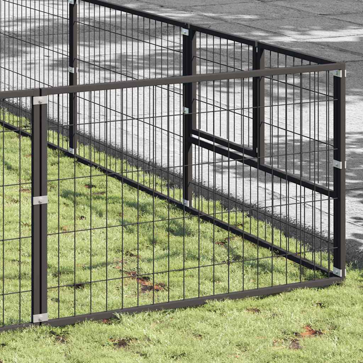 Ein dunkler Metallzaun auf Gras und asphaltiertem Untergrund.