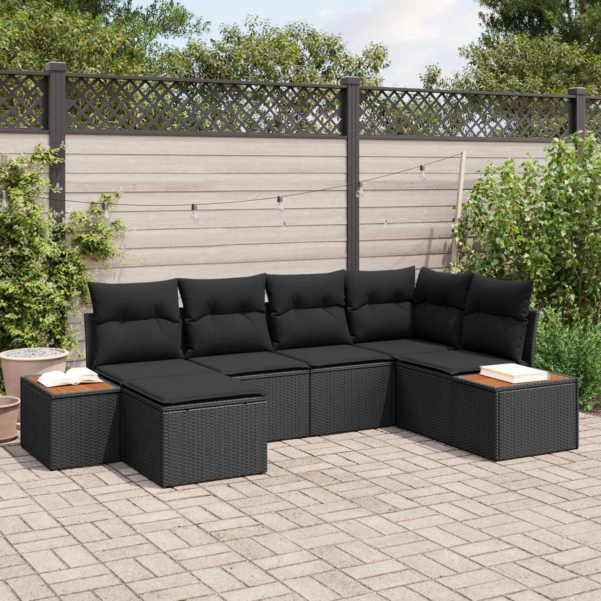 Ein schwarzes Rattan-Sofa mit Kissen auf einer gepflasterten Terrasse.
