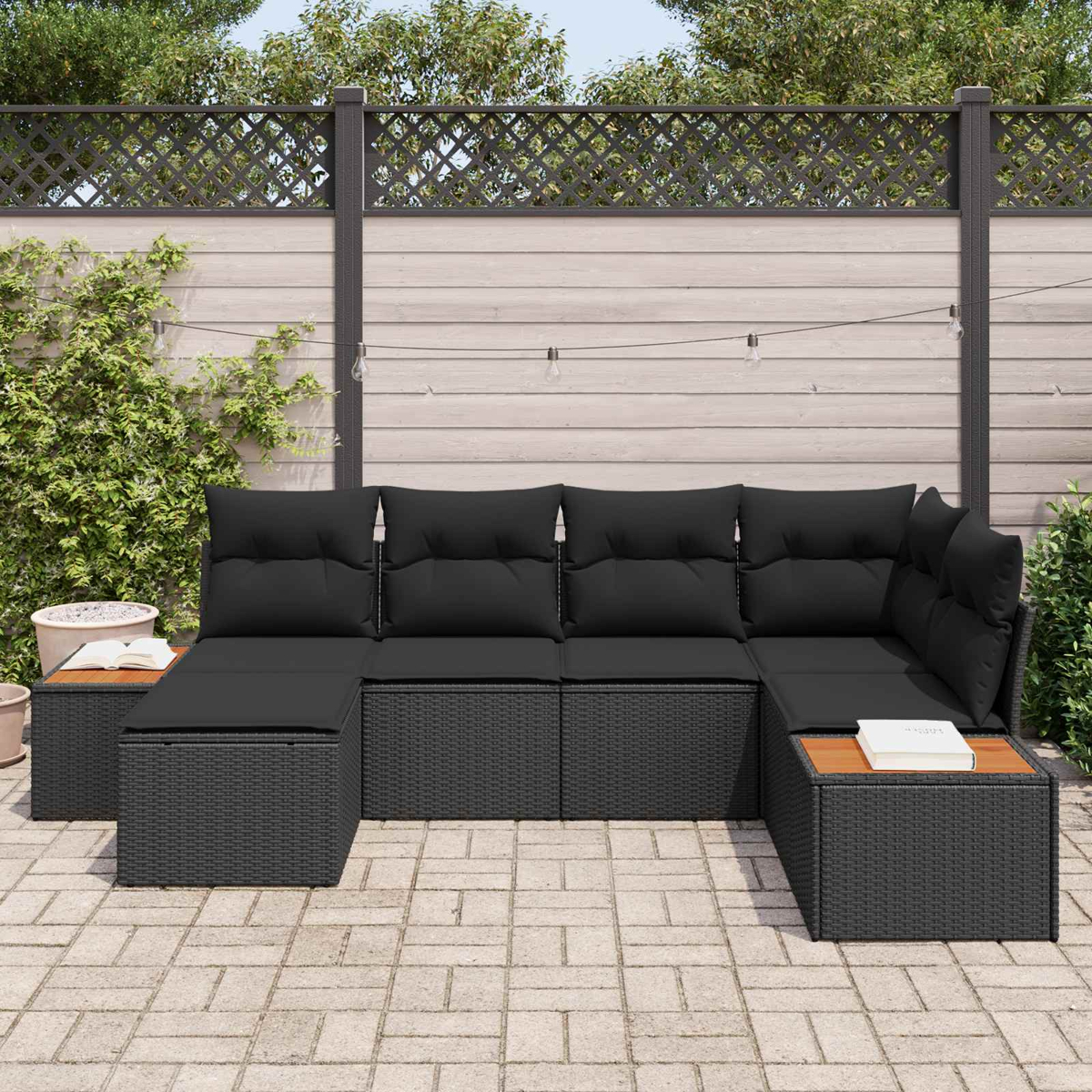 Ein schwarzes Rattan-Sofa mit Kissen steht auf einer gepflasterten Terrasse.
