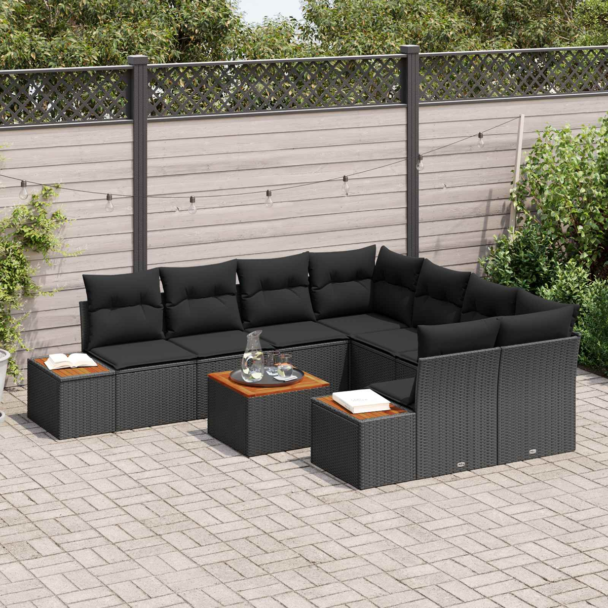 Dunkelgraues Rattan-Lounge-Set mit schwarzen Kissen auf einer gepflasterten Terrasse.