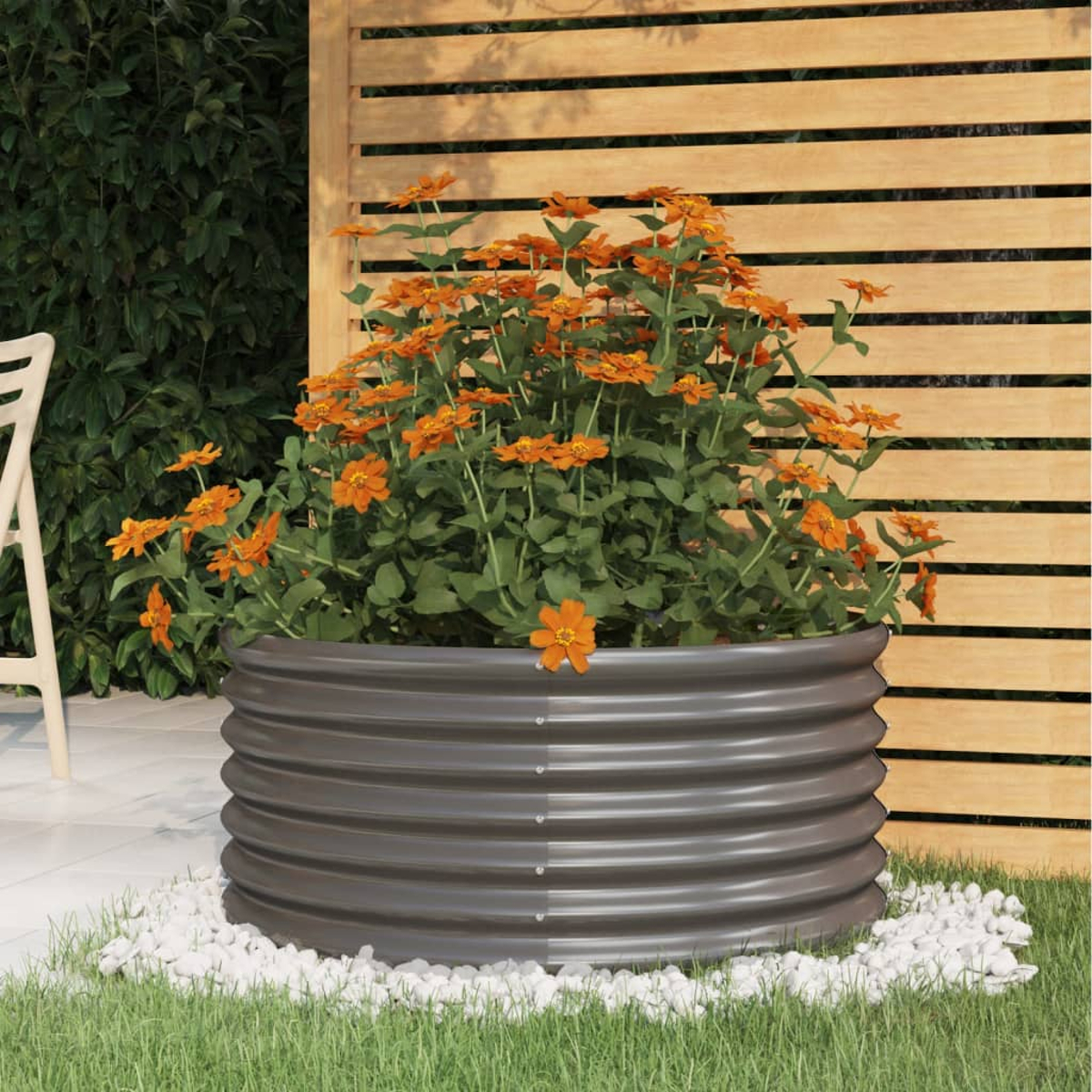 Ein grauer Wellblechpflanzer quillt über mit leuchtend orangefarbenen Blumen und grünen Blättern.