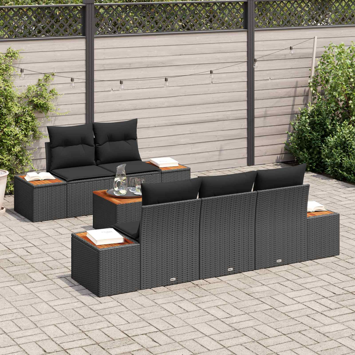Conjunto de muebles de ratán gris oscuro con cojines negros en un patio de piedra.