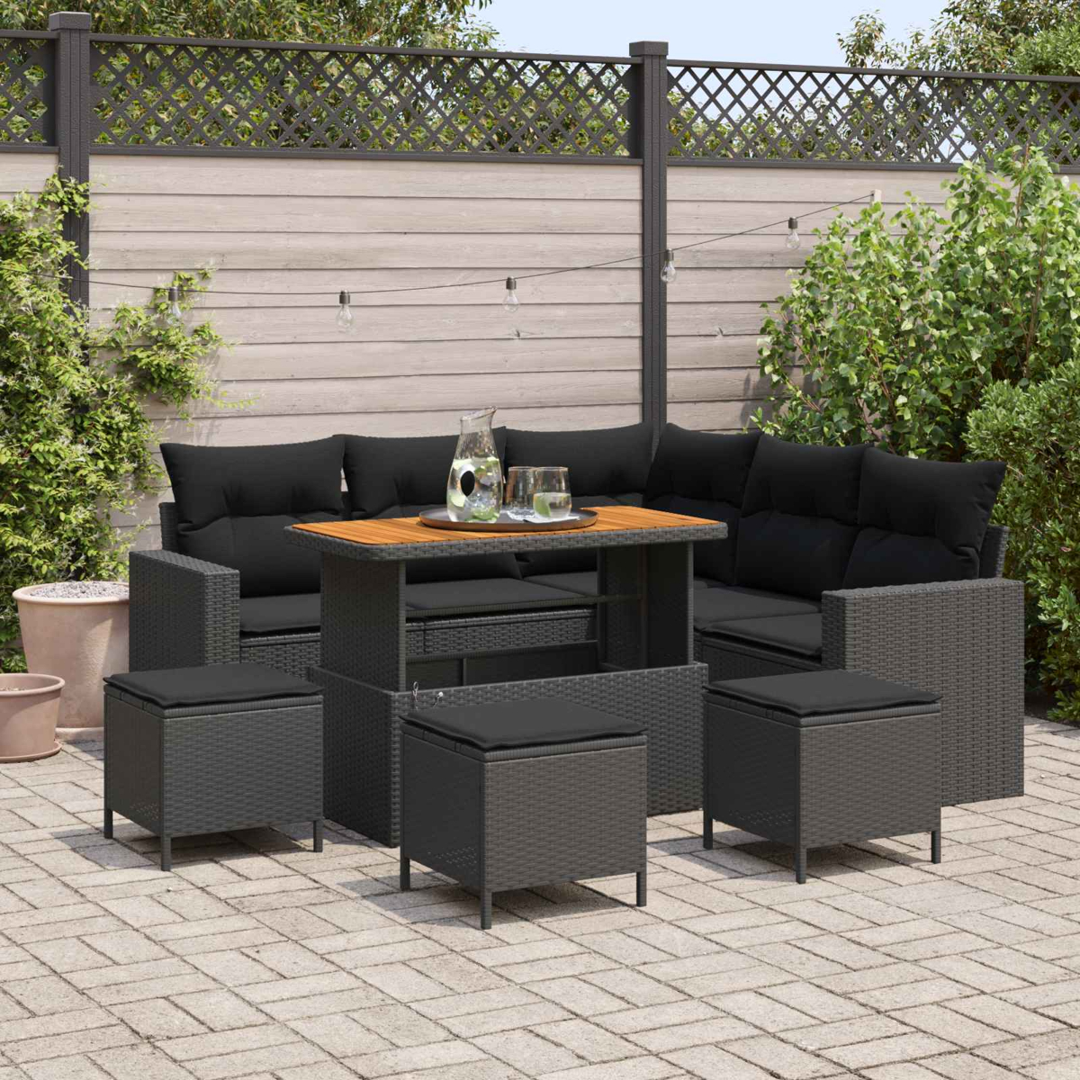 Ein Gartenmöbel-Set aus Rattan mit schwarzen Kissen, Tisch und Hockern.