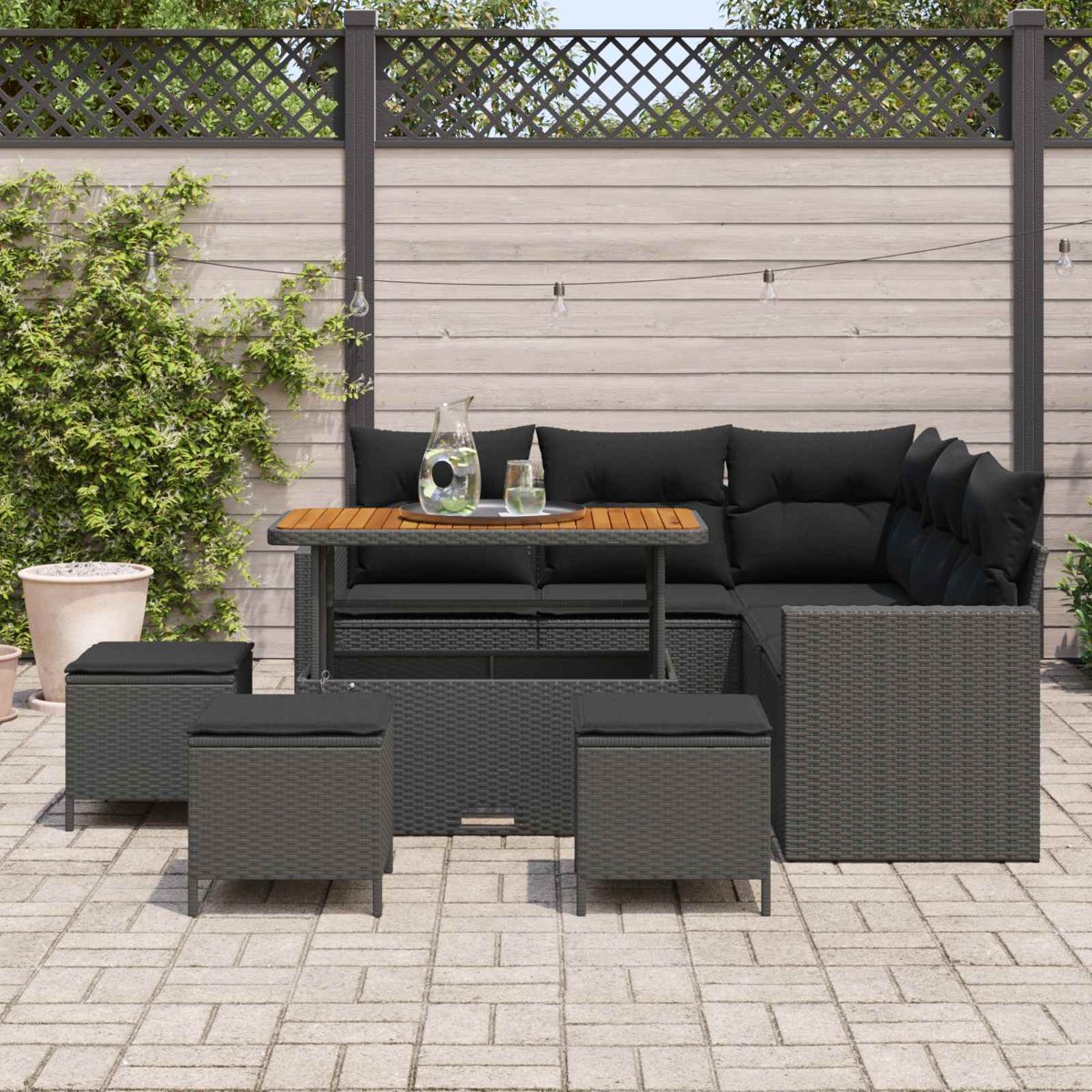 Ein dunkles Outdoor-Sofa mit Kissen, Tisch und Hockern auf einer Steinterrasse.