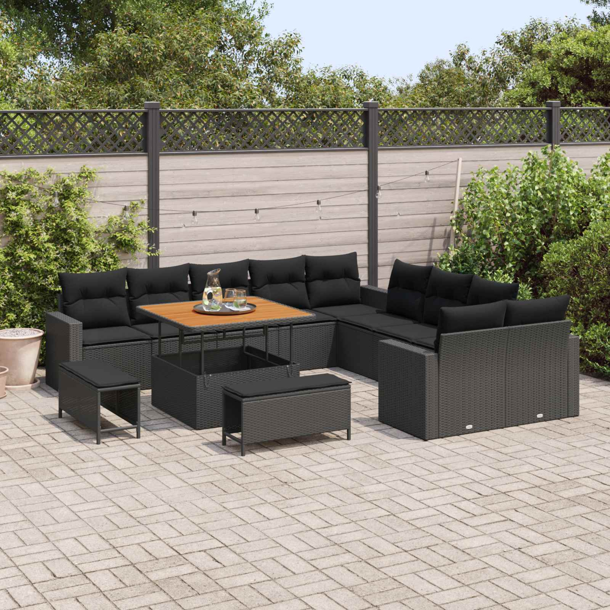 Outdoor-Rattansofa mit schwarzen Kissen und Couchtisch auf gepflasterter Terrasse.
