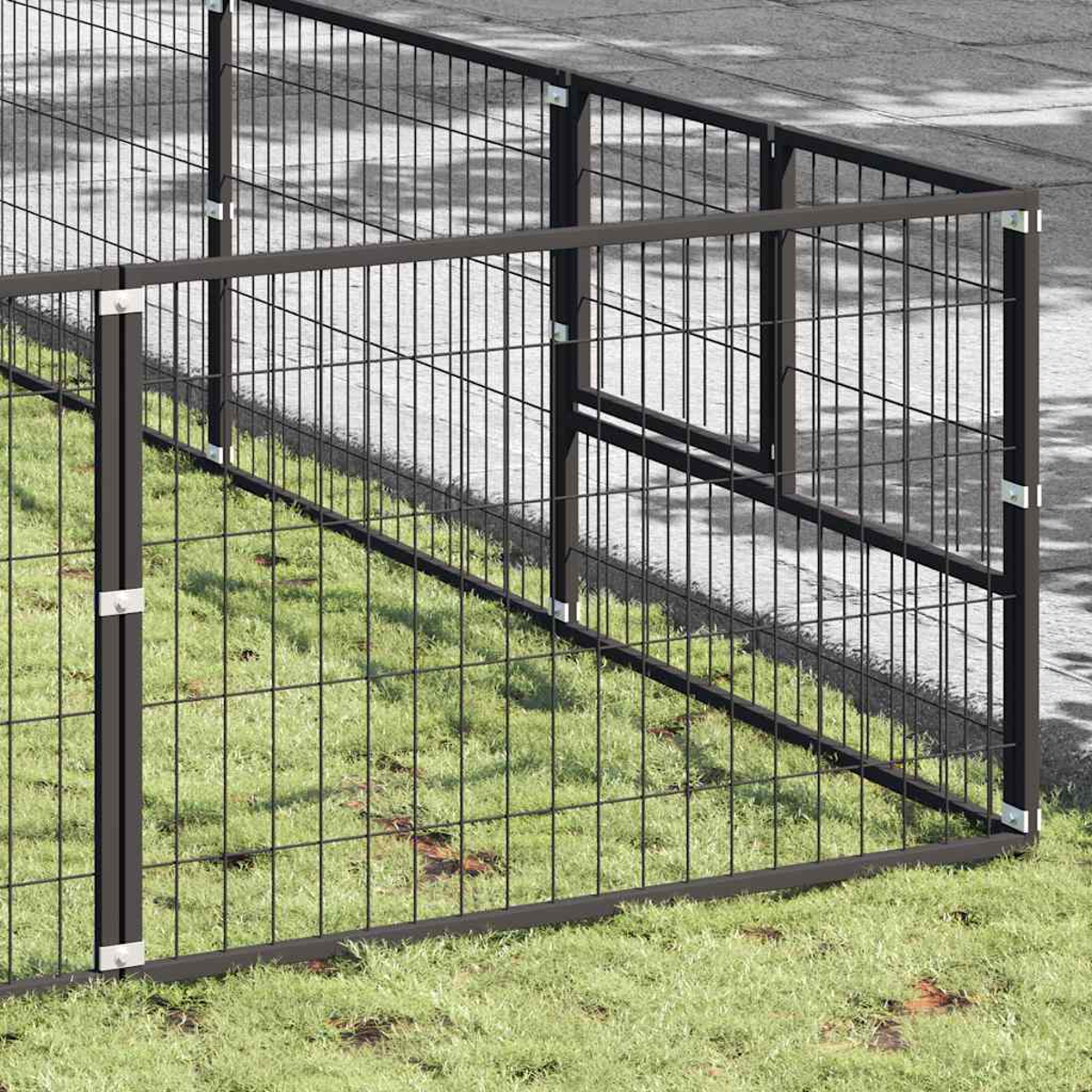 Ein schwarzer Metallzaun auf grünem Gras neben einer asphaltierten Fläche.
