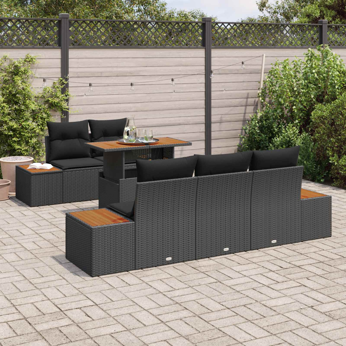 Graues Rattan-Möbelset mit schwarzen Kissen auf einer gepflasterten Terrasse.