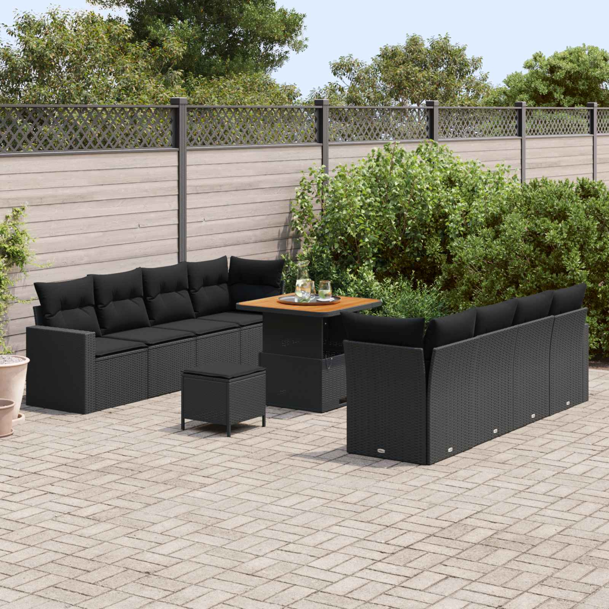 Schwarze Rattan-Lounge-Möbel mit Tisch und Hockern auf einer gepflasterten Terrasse.