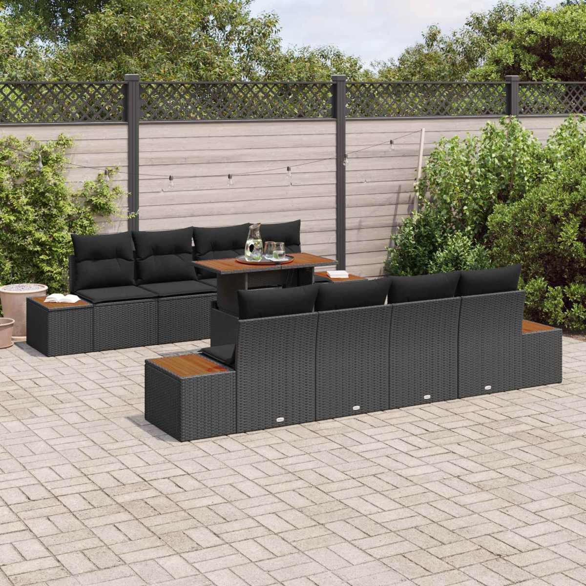 Dunkle Rattan-Gartenmöbel mit schwarzen Kissen auf einer Pflasterterrasse.