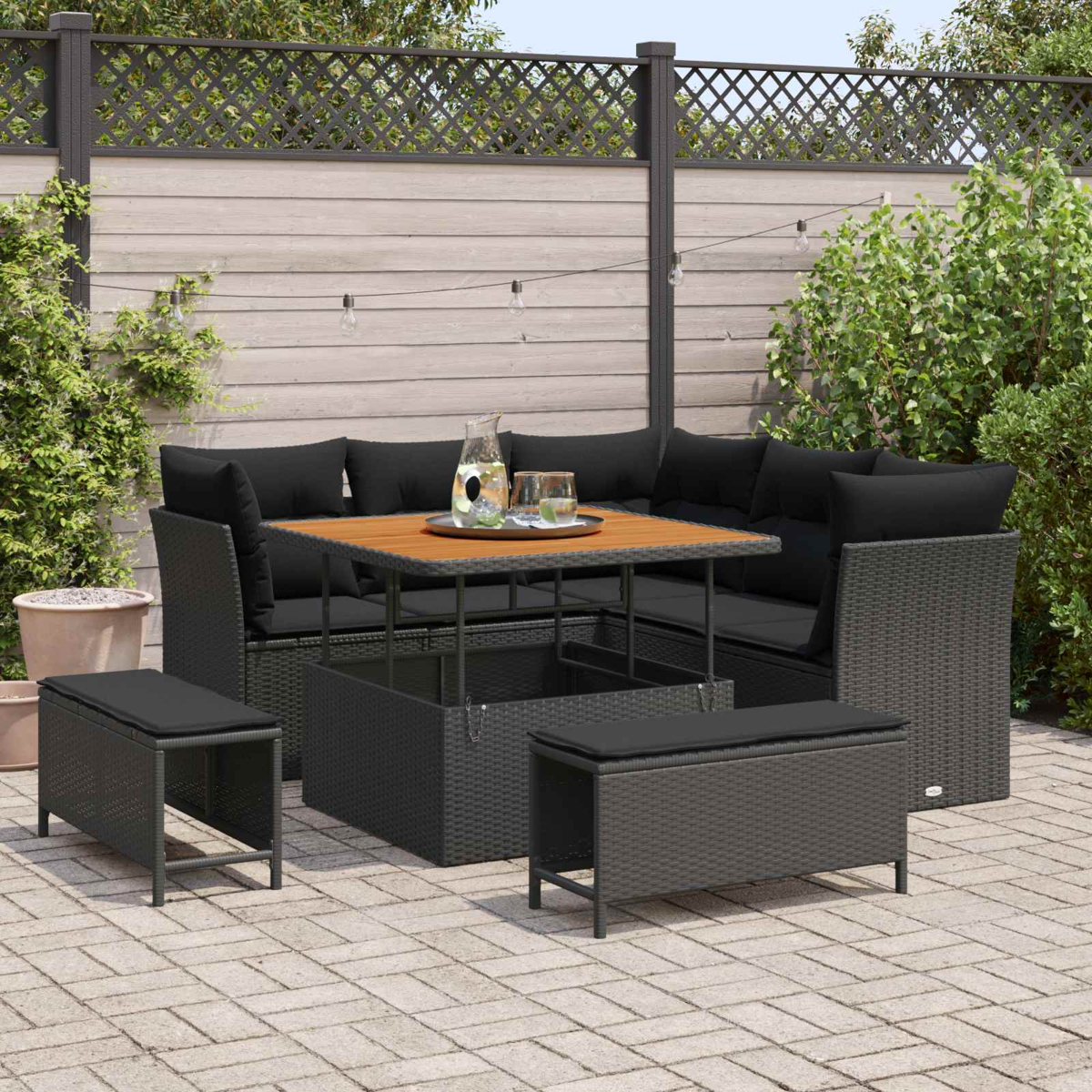 Conjunto de salón de ratán gris con mesa, cojines y dos taburetes en un patio.