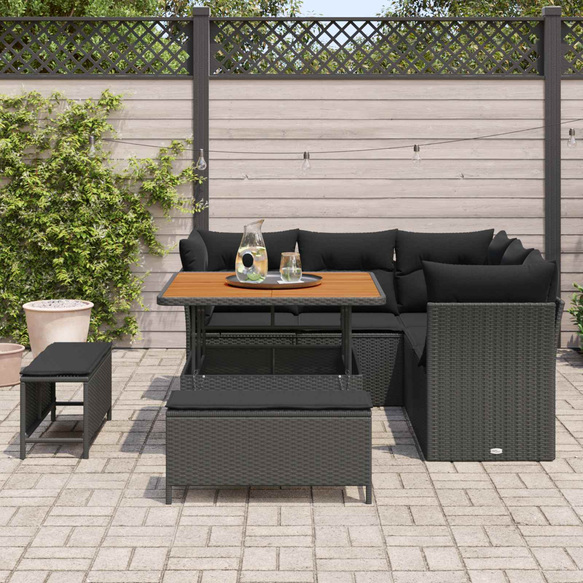 Muebles de jardín oscuros de ratán con mesa, sofá y taburetes en un patio.