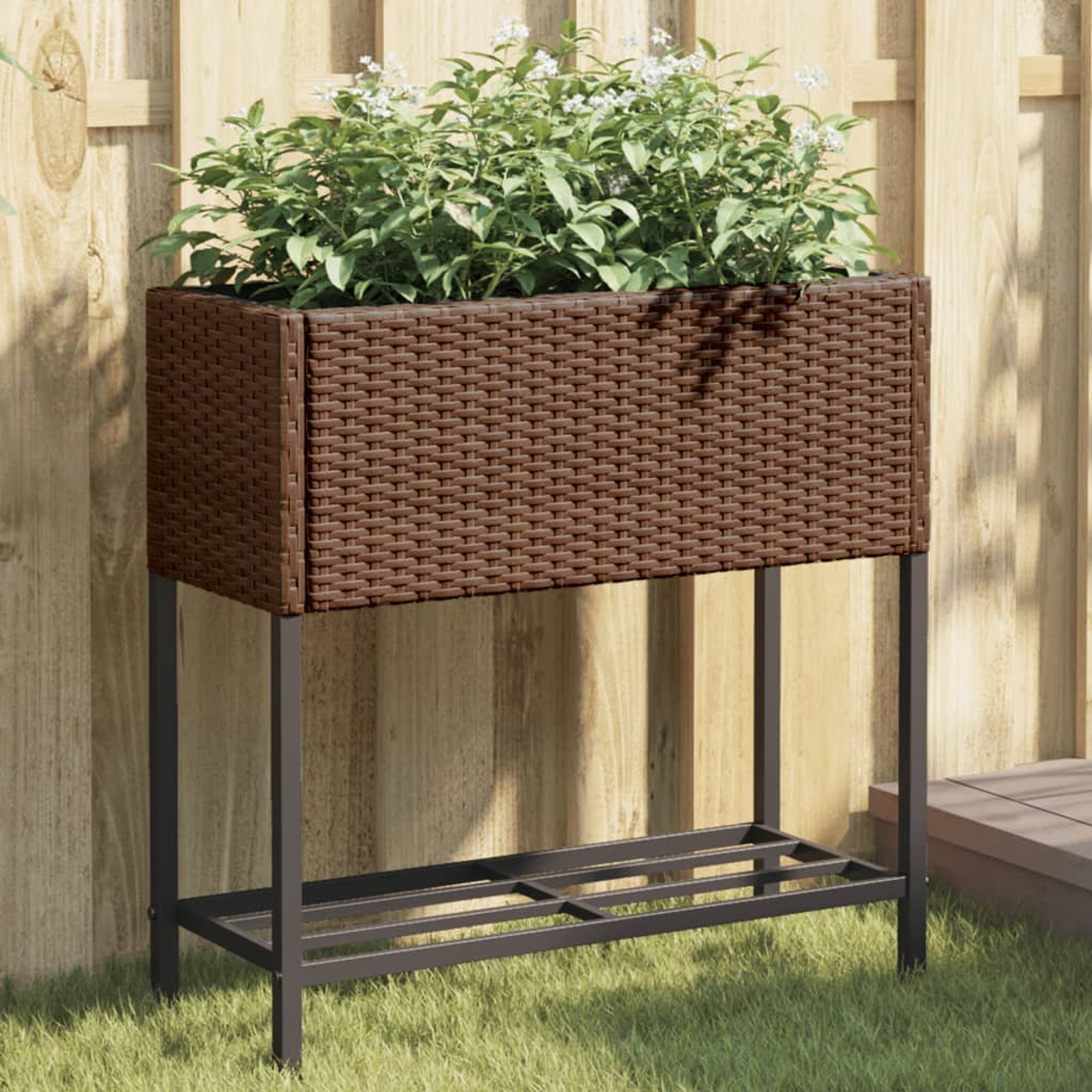 Una fioriera marrone in rattan con piante verdi su un supporto metallico davanti a una recinzione di legno.