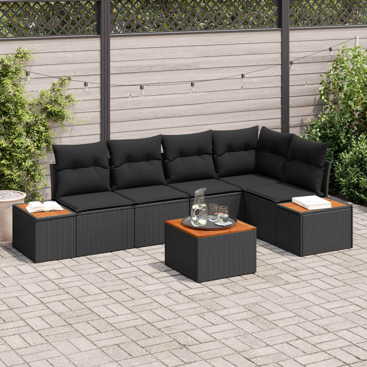 Moderne schwarze Rattan-Lounge-Ecke mit Holztisch, Kanne und Gläsern.