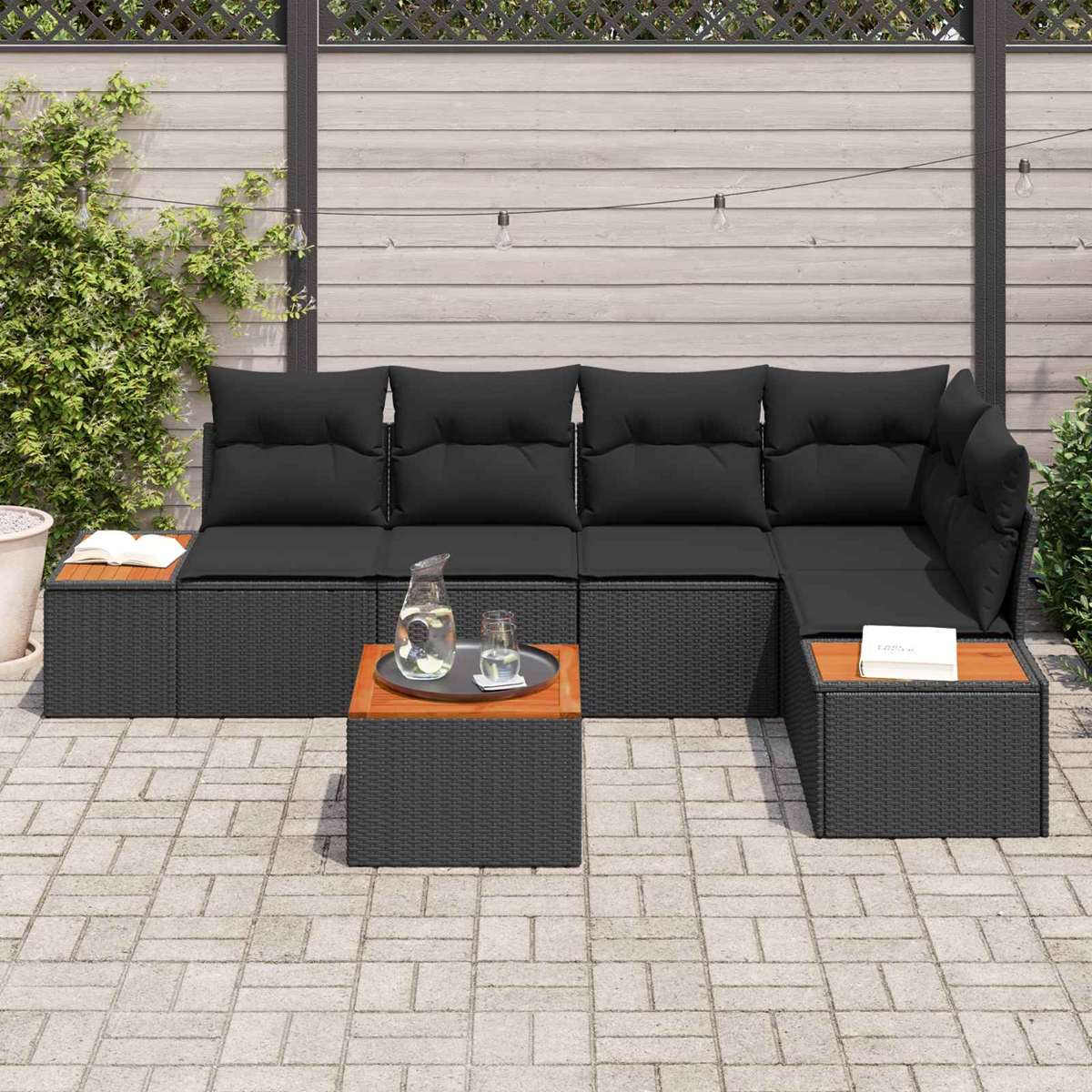 Ein dunkles Outdoor-Sofa mit Kissen und Beistelltischen auf einer Pflasterfläche.