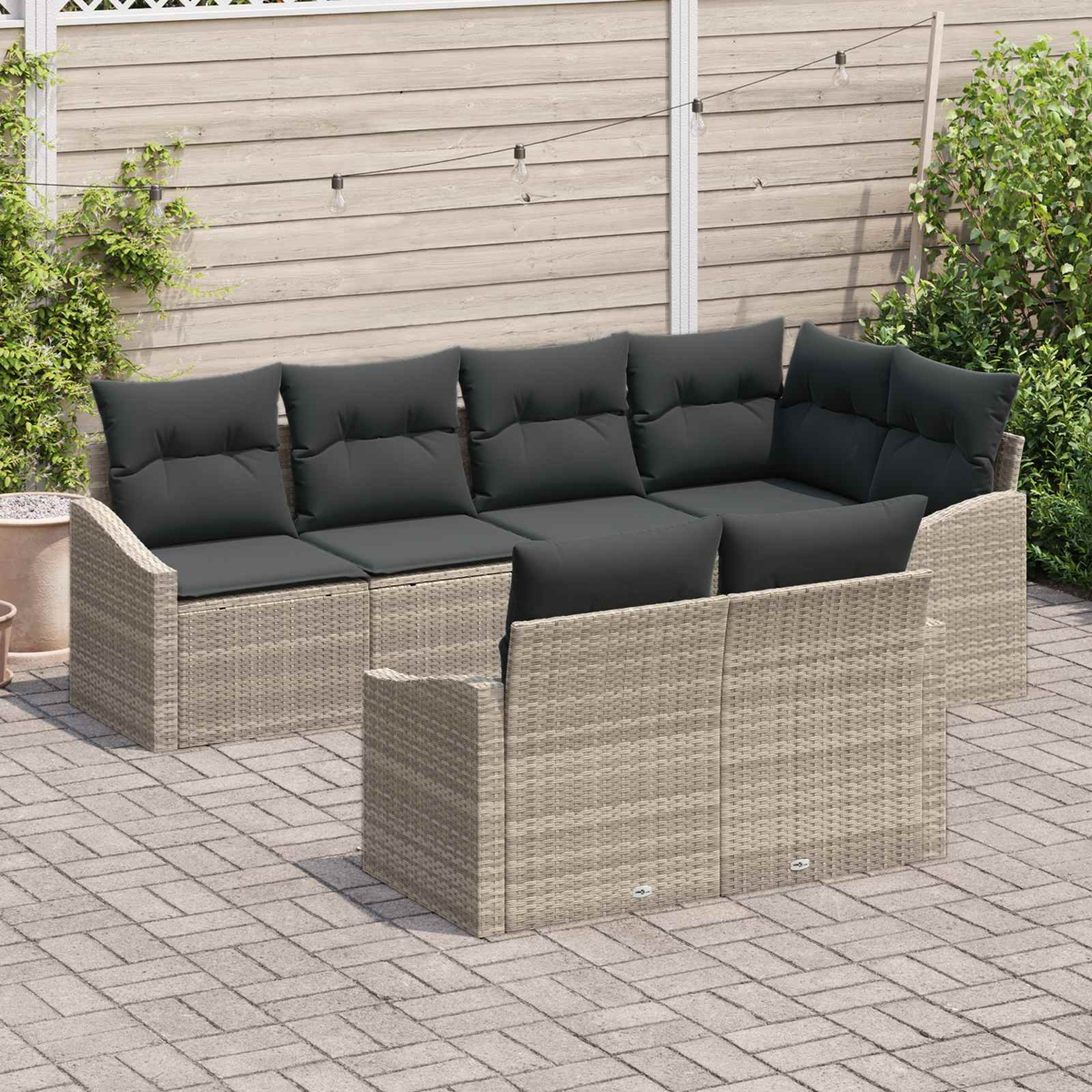 Graues Lounge-Set mit dunklen Kissen auf einer gepflasterten Terrasse.