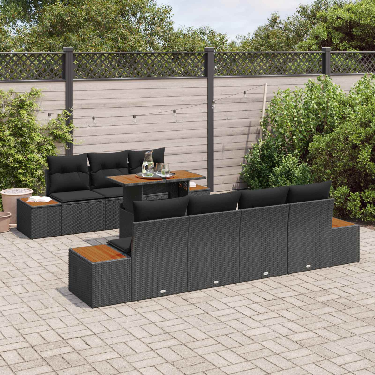 Mobiliario de salón de ratán gris oscuro con cojines negros en un patio pavimentado.