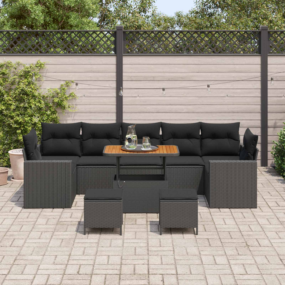 Dunkelgraues Rattan-Gartenmöbel-Set mit schwarzen Kissen auf gepflastertem Hof.