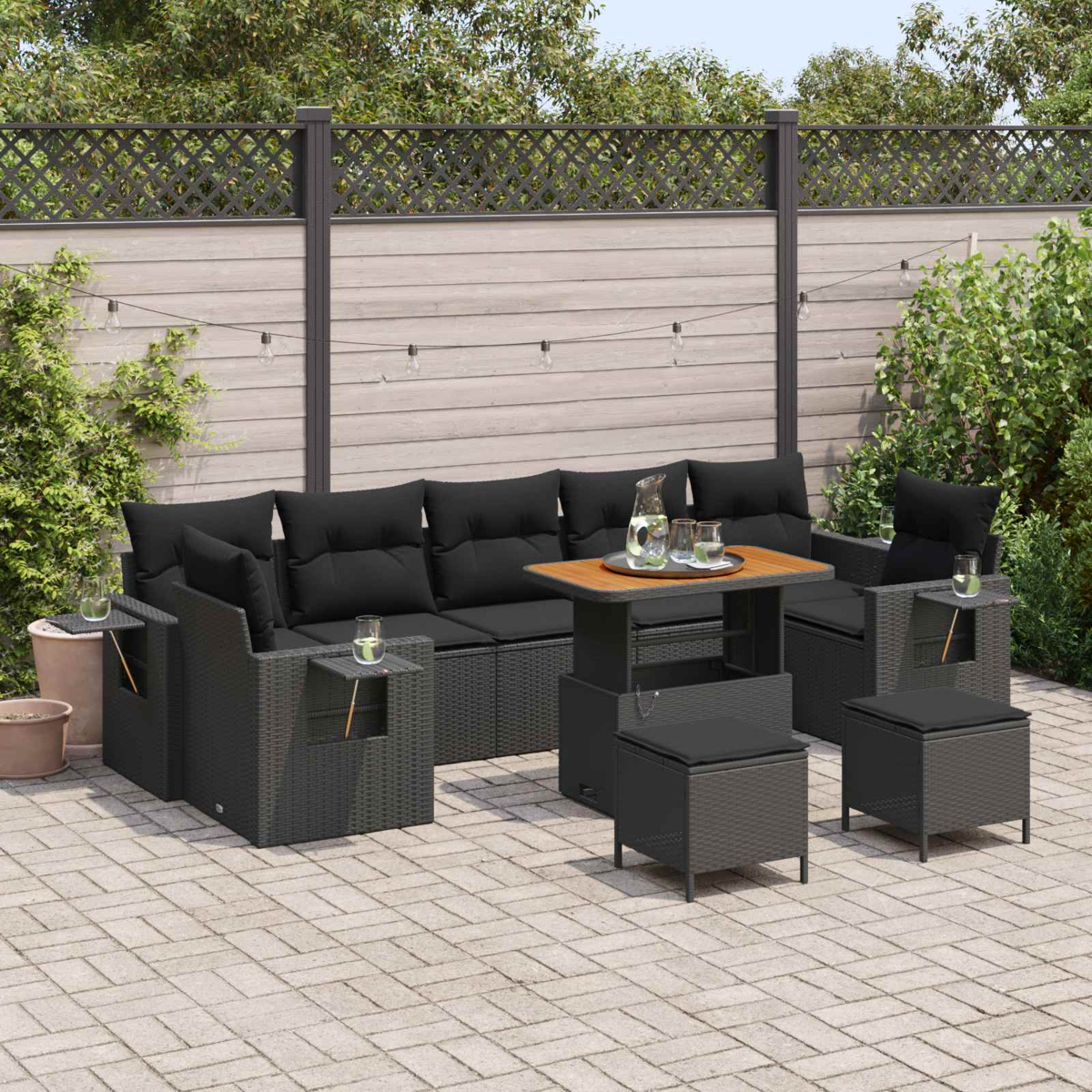 Dunkelgraue Rattansofa-Garnitur mit schwarzen Kissen auf gepflasterter Terrasse.