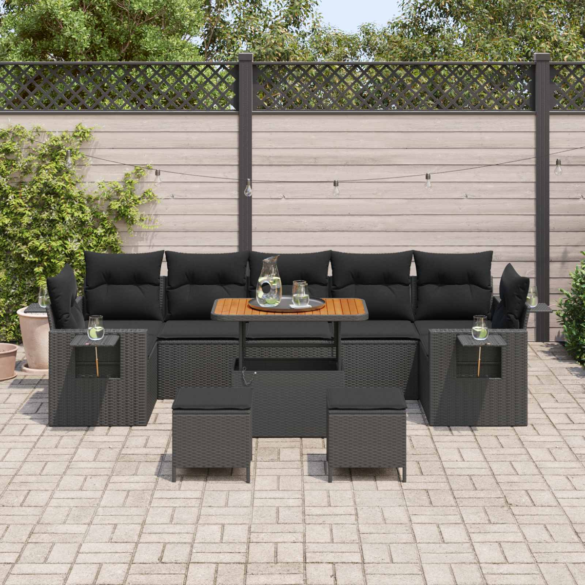 Graues Rattan-Lounge-Set mit schwarzen Kissen und Hockern auf einer Steinterrasse.
