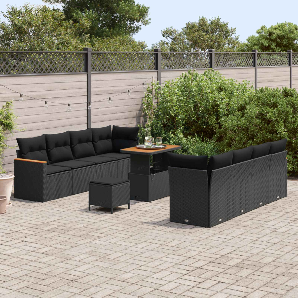 Ein schwarzes Rattan-Sofa mit Kissen, ein Tisch und ein Hocker auf einer Terrasse.
