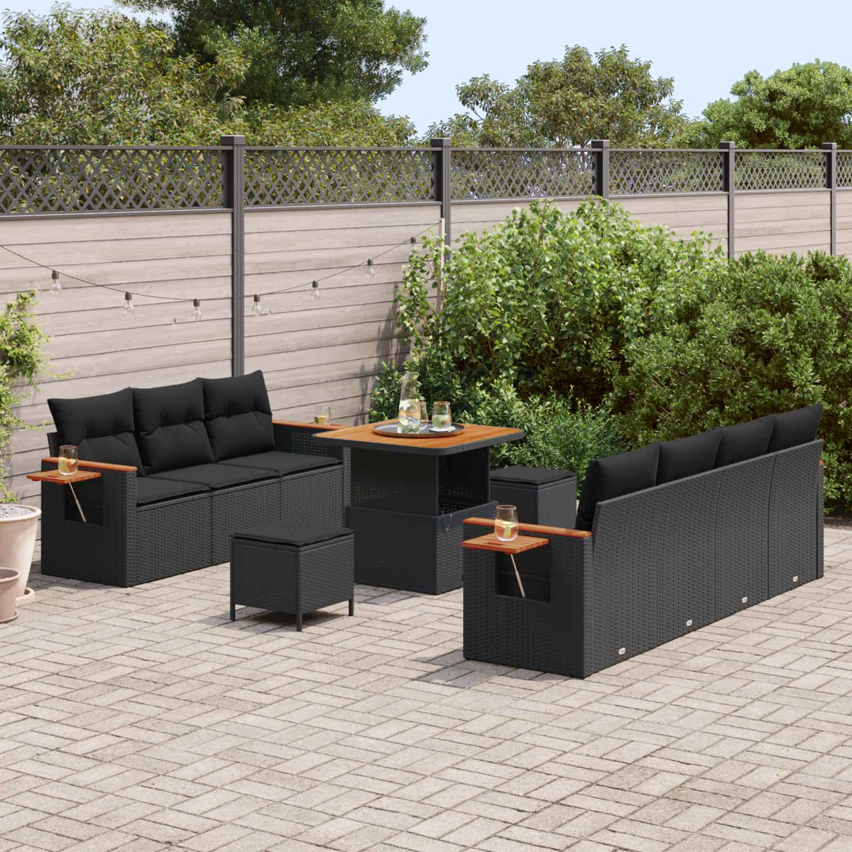 Gartenmöbel-Set aus schwarzem Rattan mit Kissen, Tisch und Hockern auf einer gepflasterten Terrasse.