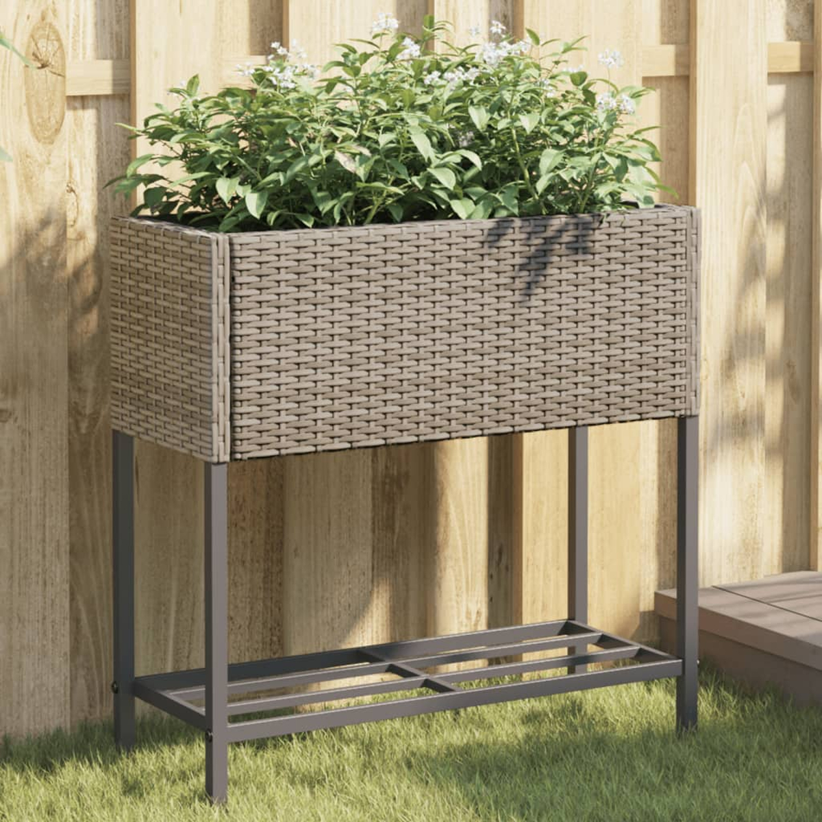 Una fioriera rialzata in rattan con piante si trova davanti a una staccionata di legno.