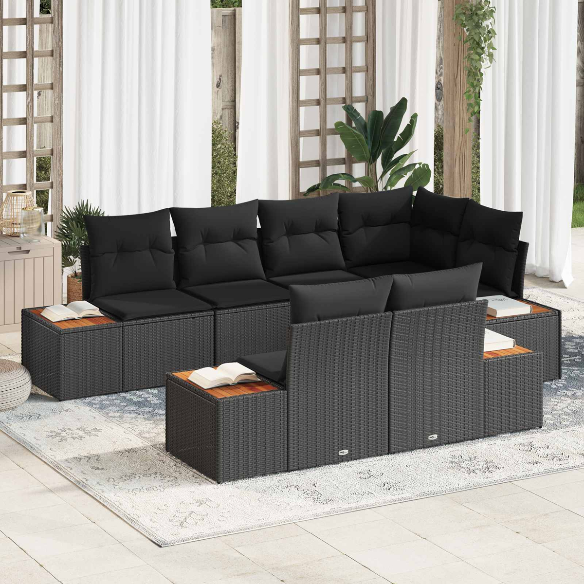 Dunkelgraues Rattan-Sofa mit schwarzen Kissen auf einer Terrasse mit weißem Teppich.
