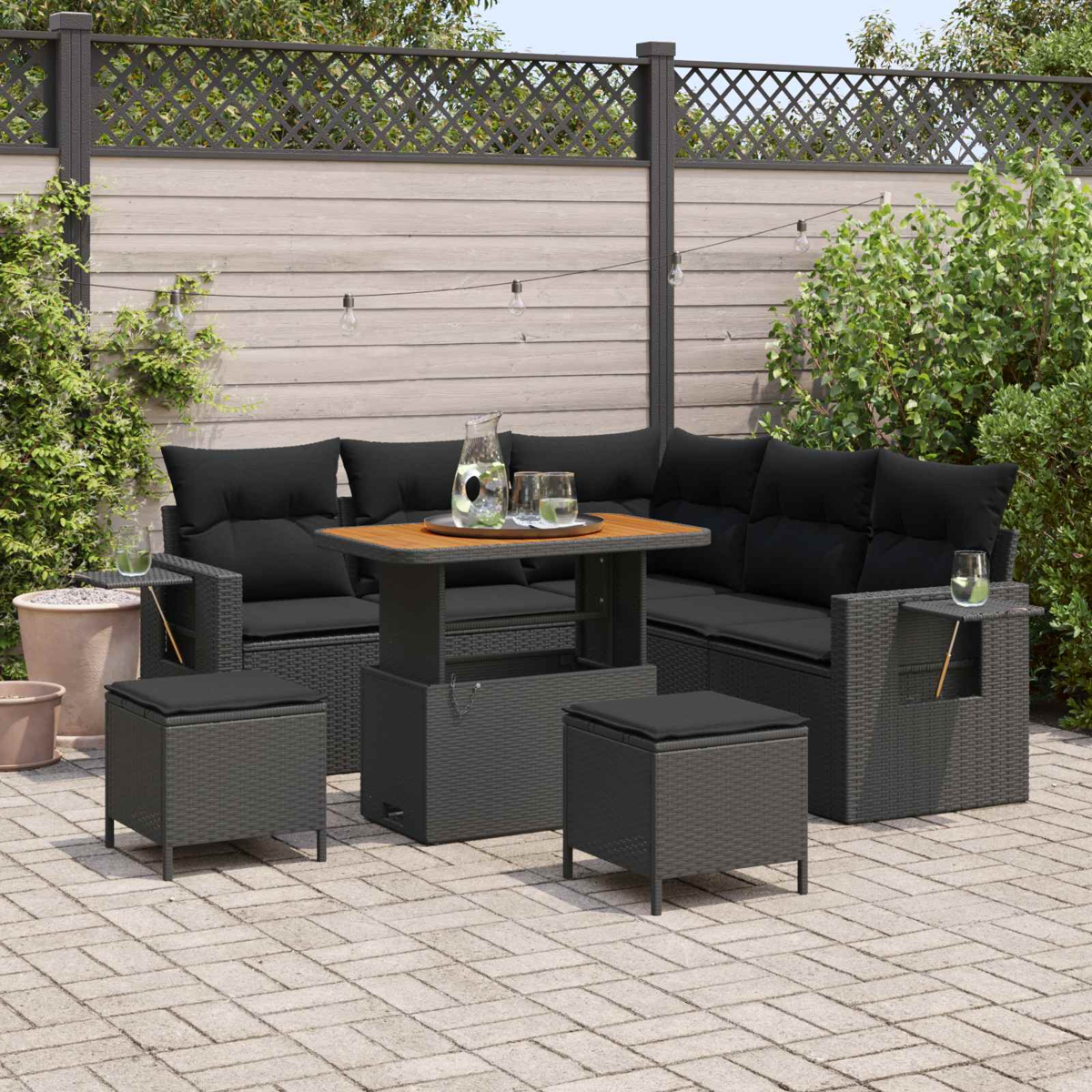 Conjunto de salón de ratán gris oscuro con cojines negros, mesa y taburetes en patio.