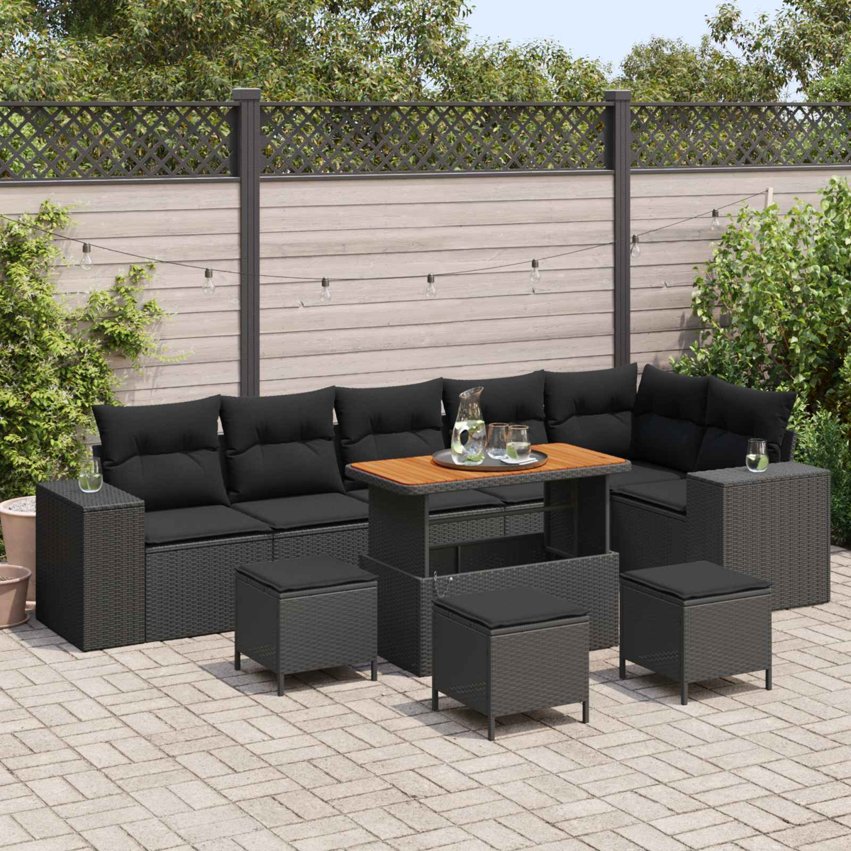 Ein graues Rattan-Sofa mit schwarzen Kissen und einem Holztisch im Freien.