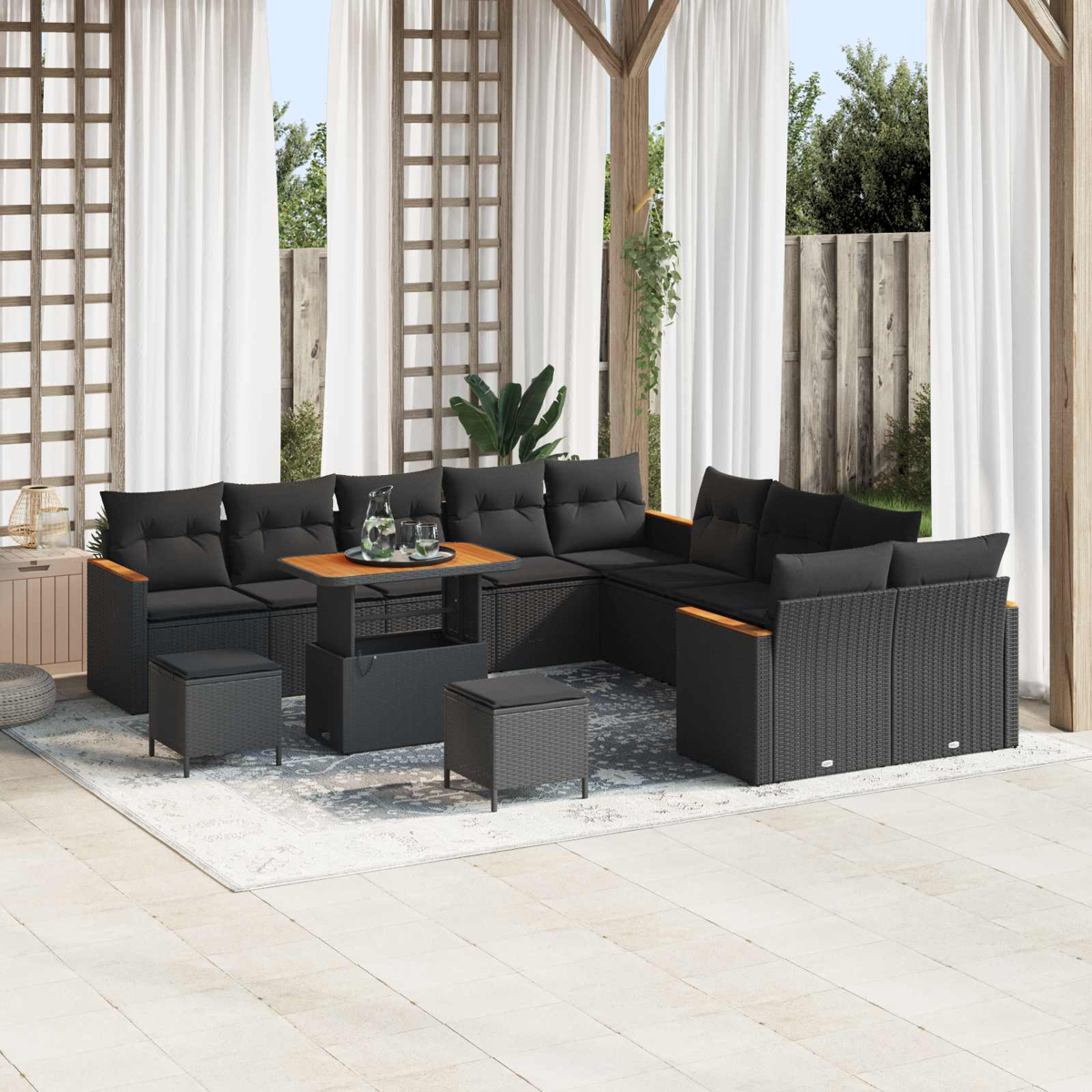 Ein schwarzes Rattan-Sofa mit Kissen, ein Couchtisch und zwei Hocker auf einer Veranda.