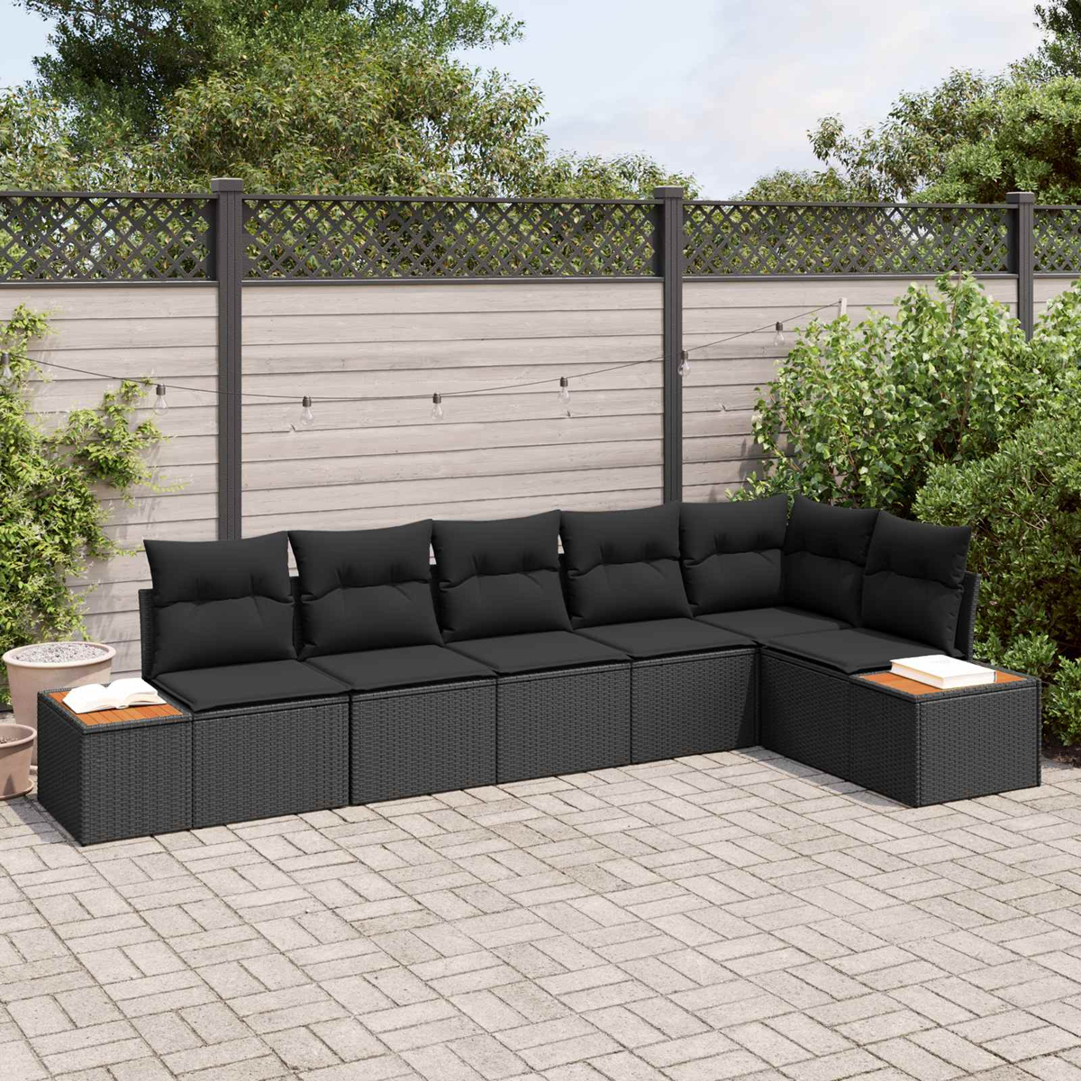 Dunkelgraues Rattansofa mit Kissen und Holzakzenten auf gepflastertem Hof.