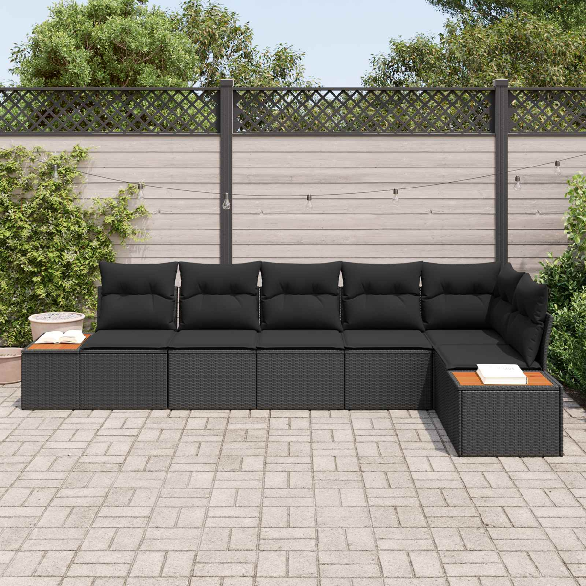 Ein modulares schwarzes Rattan-Sofa mit Kissen steht auf einer gepflasterten Terrasse.