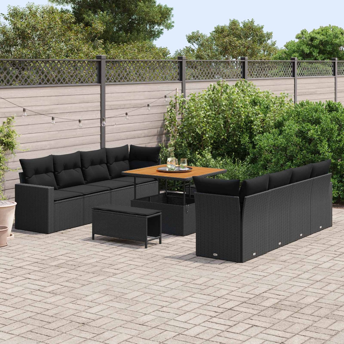 Schwarzes Outdoor-Möbelset aus Weidengeflecht mit Kissen auf einer gepflasterten Terrasse.