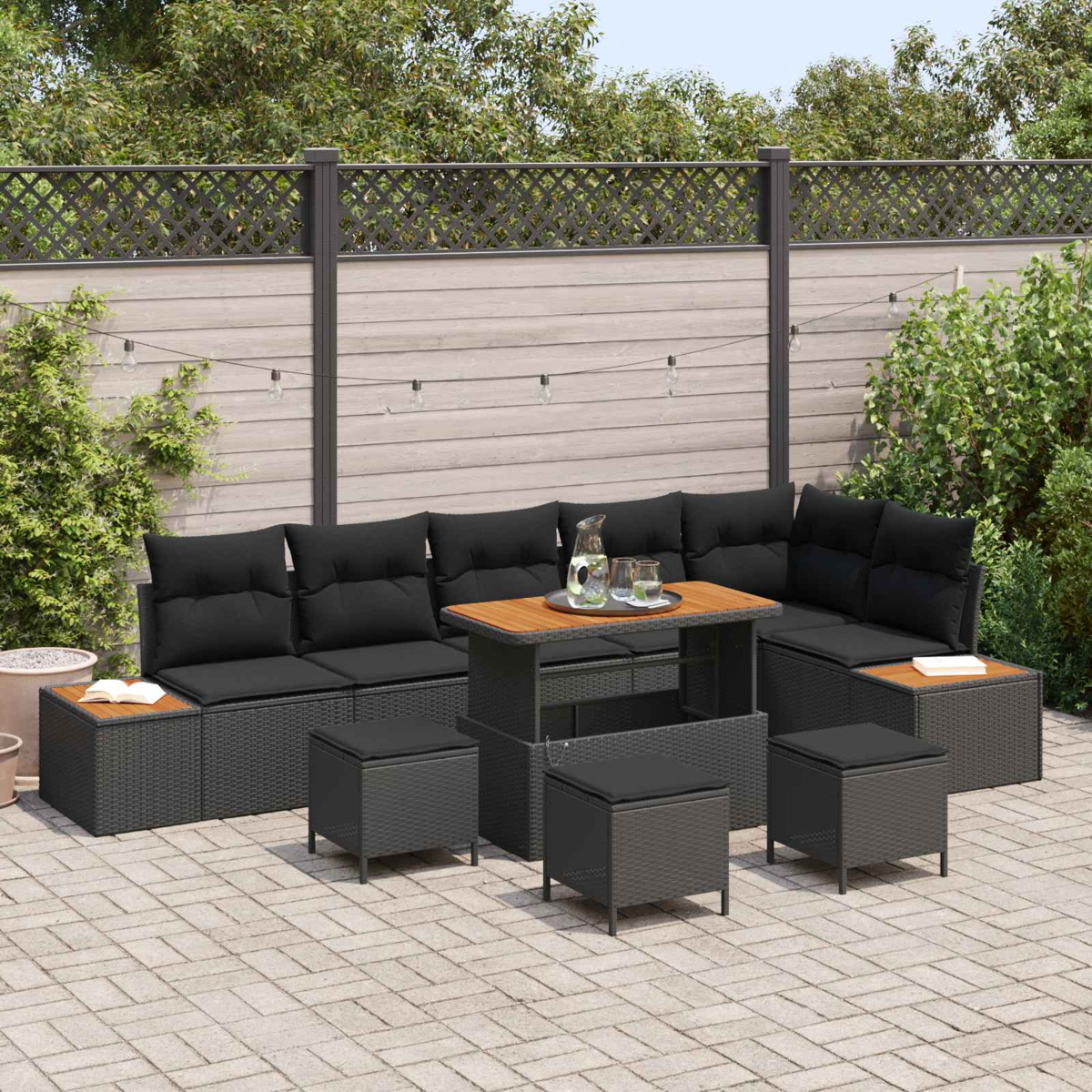 Graues Rattansofa mit schwarzen Kissen und Holztisch auf gepflastertem Hof.