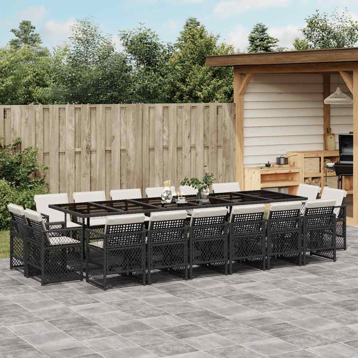 Ein großer Gartentisch mit schwarzen Stühlen und weißen Kissen steht auf einer Steinterrasse.