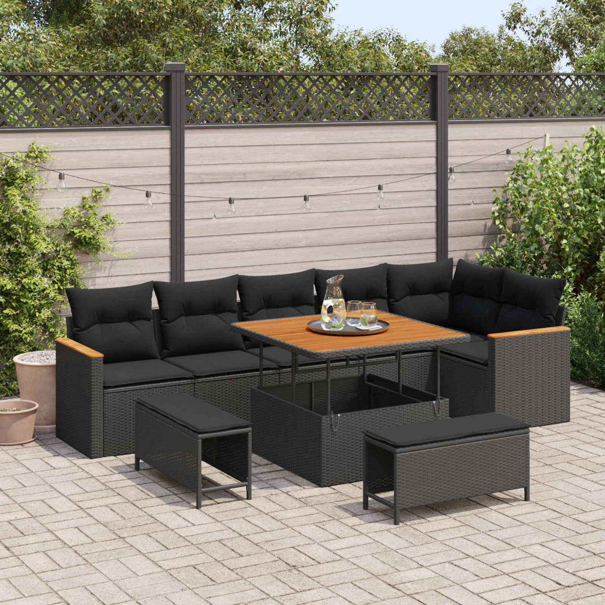 Gartenlounge mit schwarzen Kissen und Holztisch auf einer Terrasse.